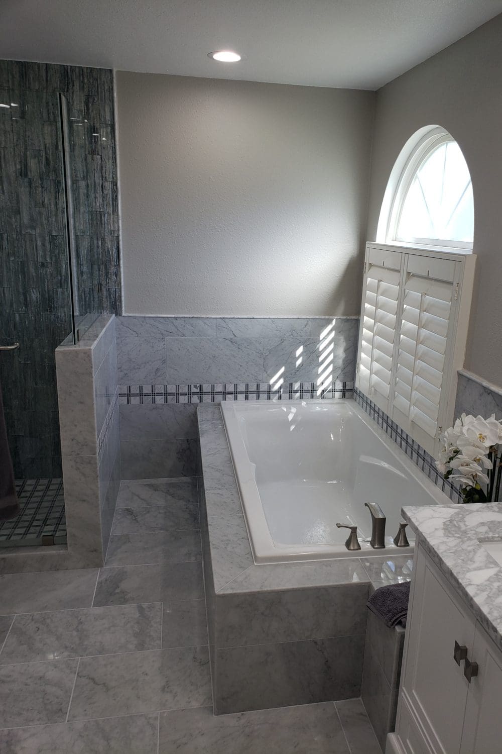 A bathroom with marble walls and floors, a tub, shower stall, and a window.