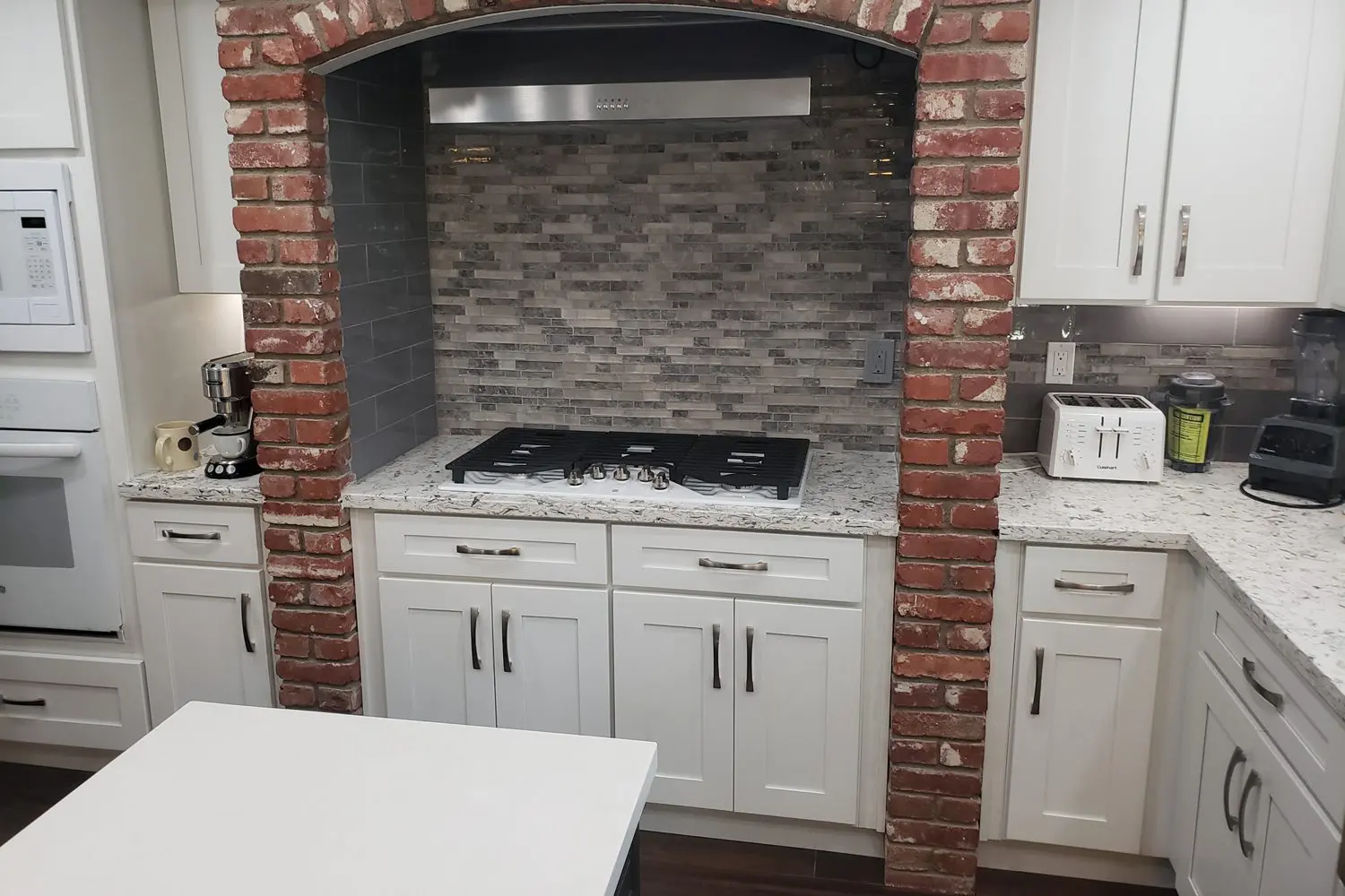 A kitchen with white cabinets and brick walls.