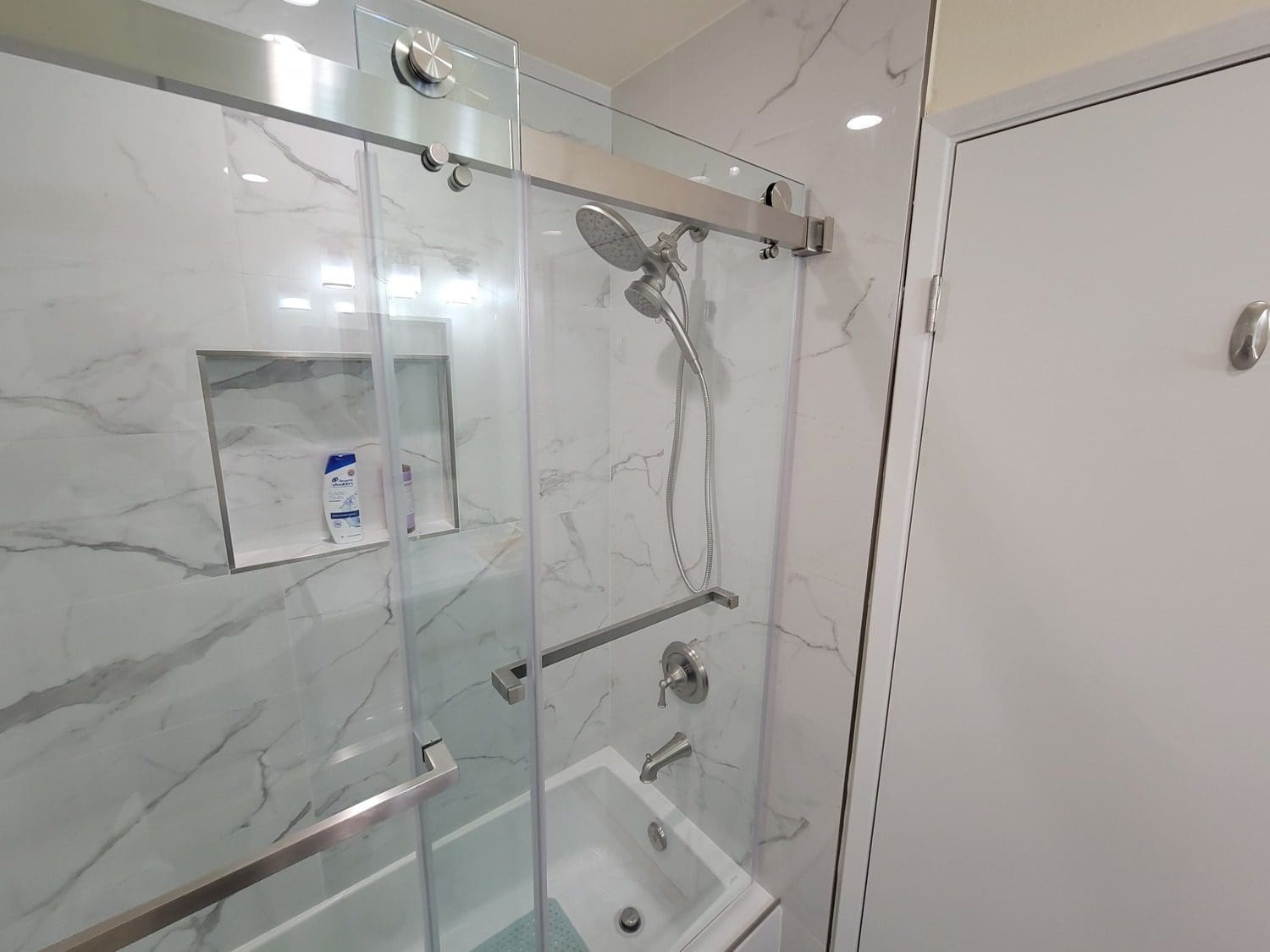 A bathroom with a glass shower door and white walls.