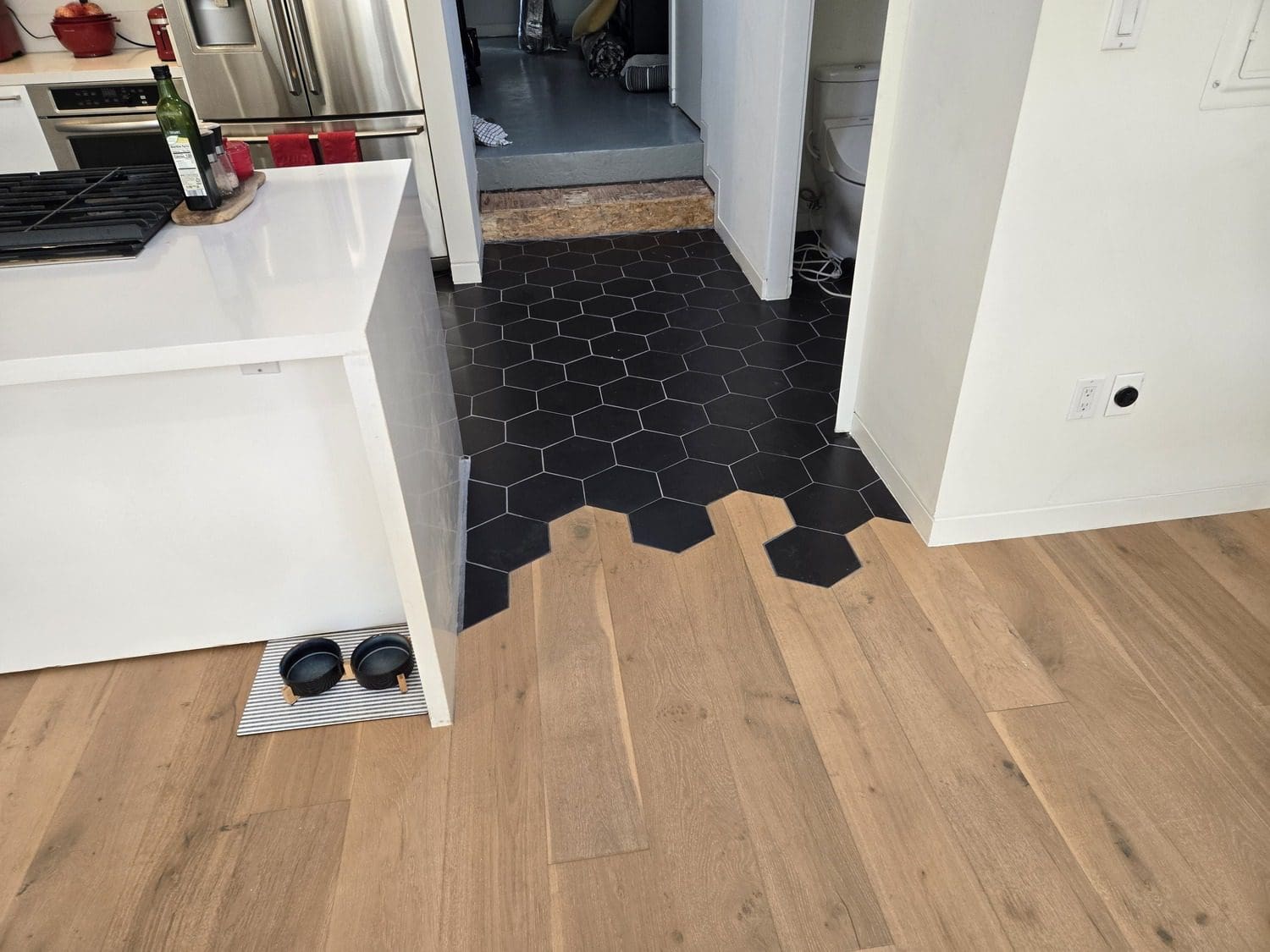 A black hexagonal tile floor in the middle of a kitchen.