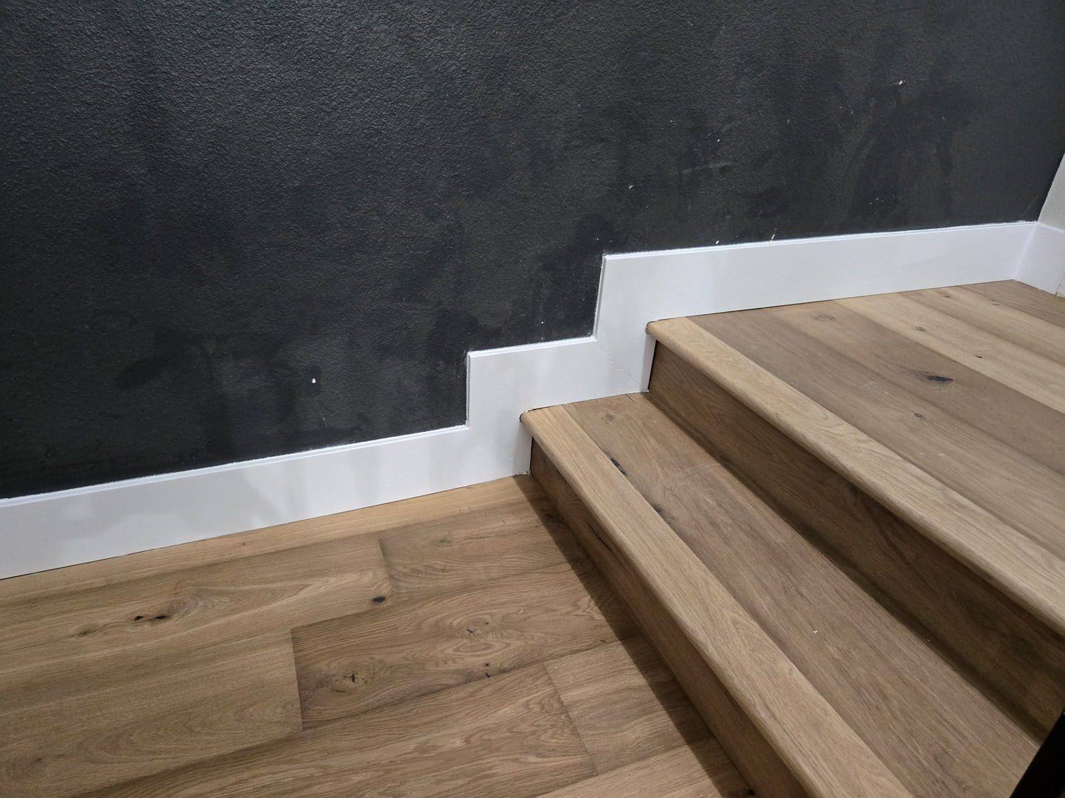 A wooden staircase with white steps and a black wall.