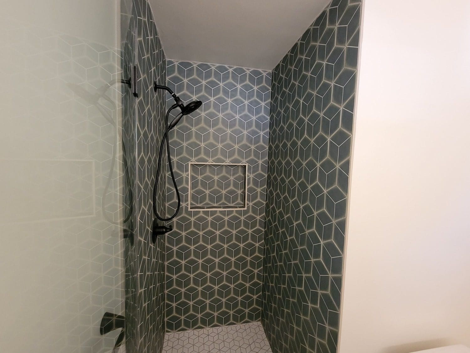 A shower with a tiled wall and a shelf