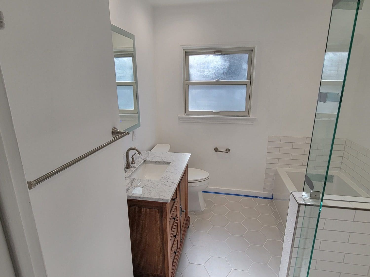 A bathroom with white tile and wood cabinets.