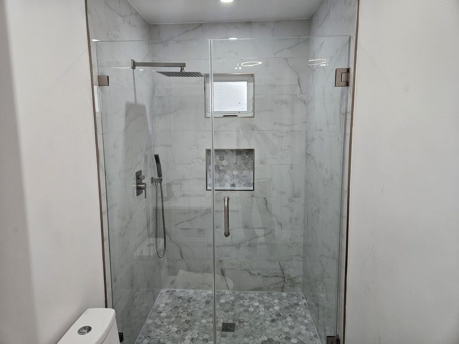 A bathroom with a glass shower door and marble tile.