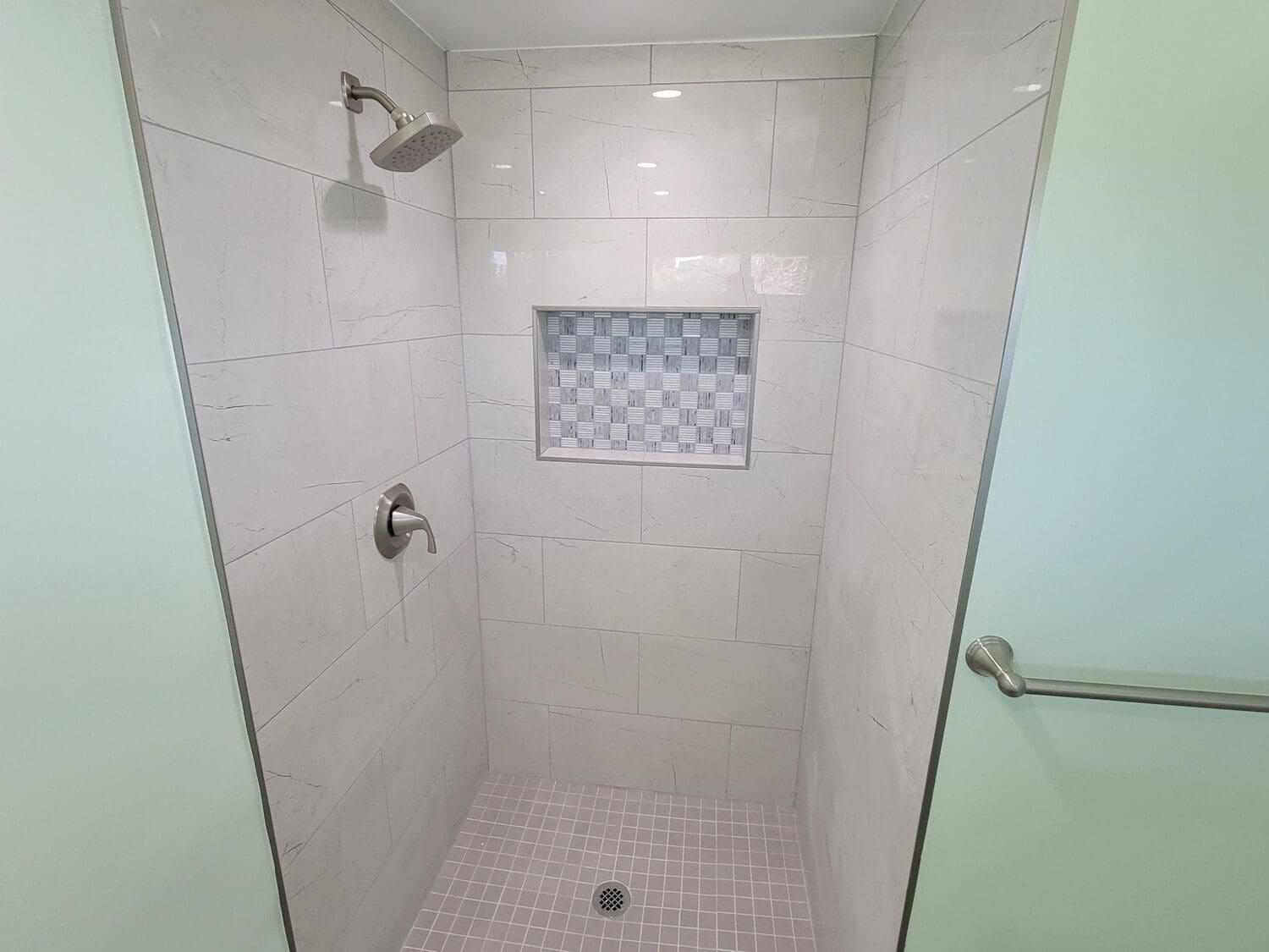 A white tiled shower with a window in the middle.