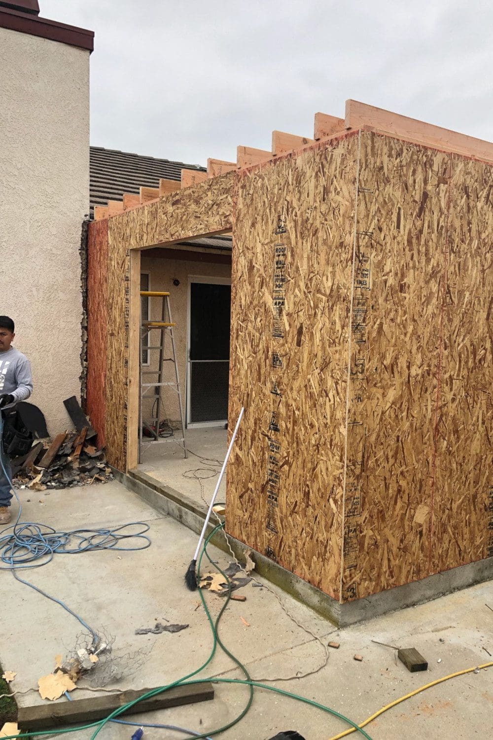 A man standing next to a building with wood shavings on the outside.