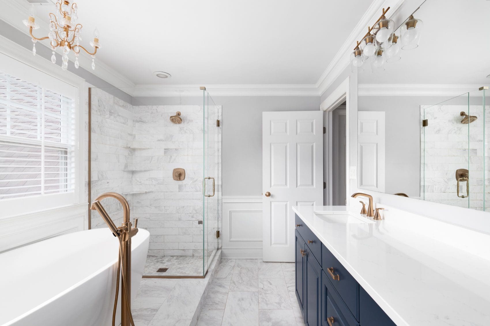 A bathroom with marble floors and walls, two sinks, and a walk in shower.